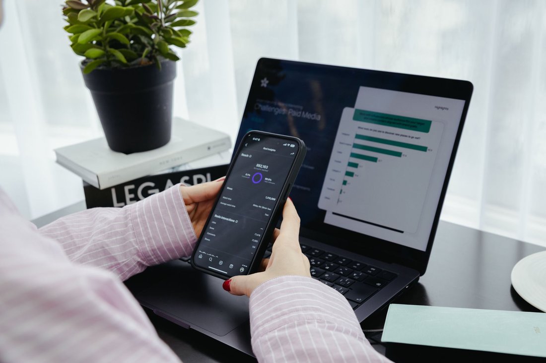 Checking reel performance and reach on a phone next to a laptop