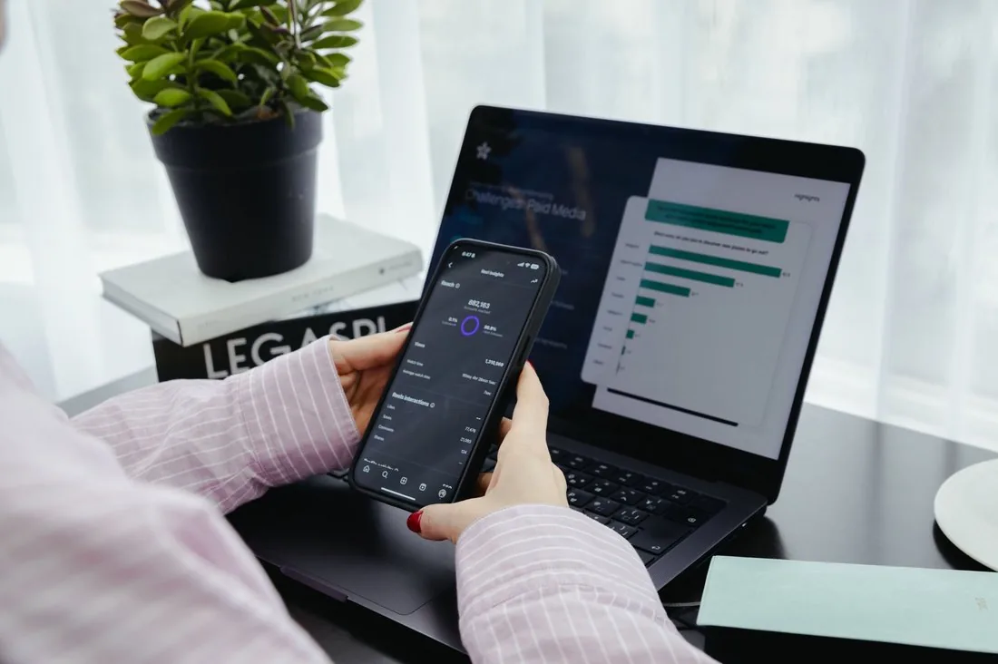 Checking reel performance and reach on a phone next to a laptop